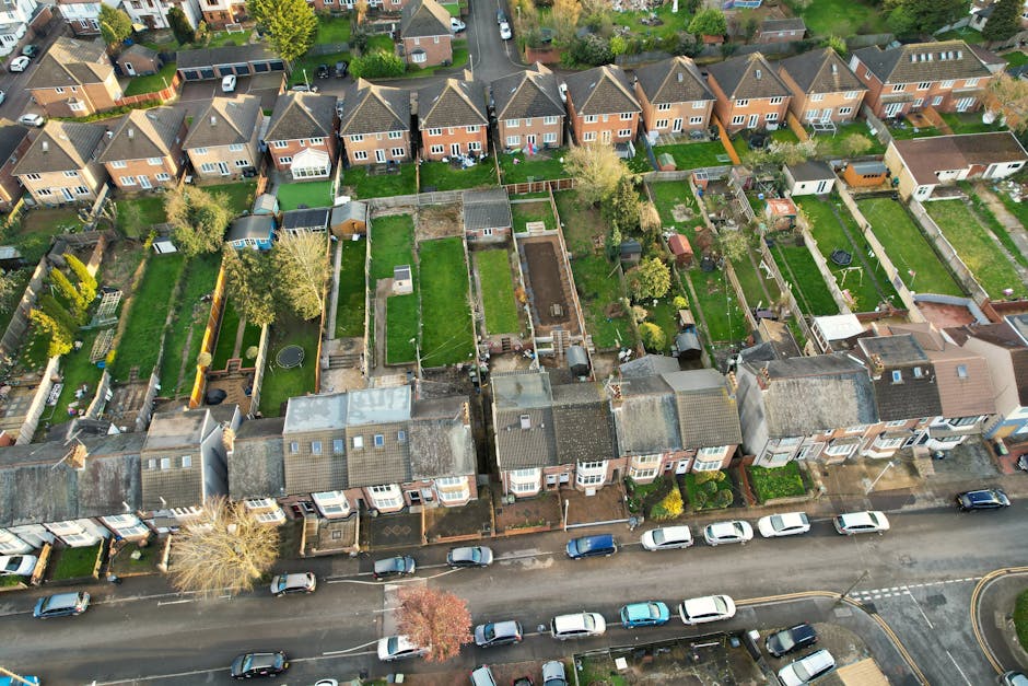 A small, well-maintained garden area in front of a white residential building featuring a central paved pathway leading to a decorative wrought iron bench positioned against the building's wall. The g